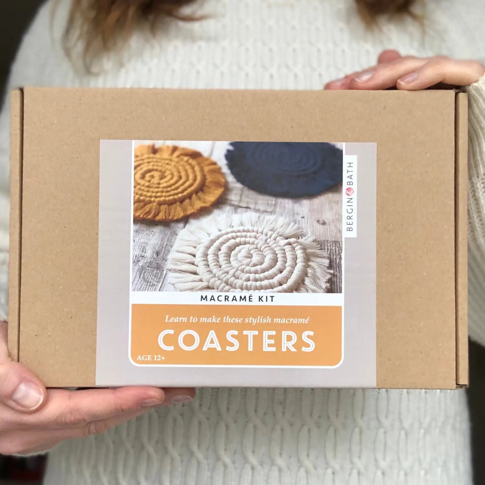 Box containing a macramé coaster kit held by a person wearing a white sweater.