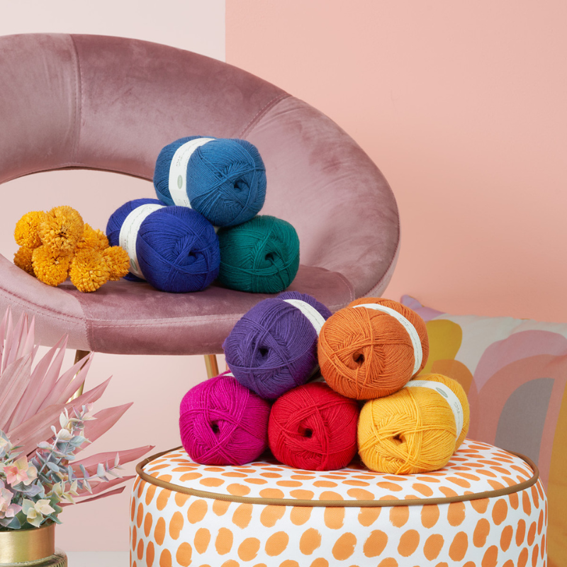 Colorful yarn balls on a chair and stool with a pink background